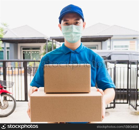 Asian delivery express courier young man use giving boxes to woman customer he wearing protective face mask at front home, under curfew quarantine pandemic coronavirus COVID-19