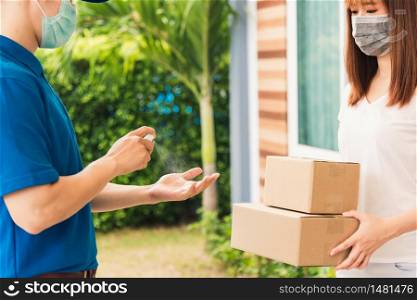 Asian delivery express courier young man use spray sterilize before giving boxes to woman customer receiving both protective face mask, under curfew quarantine pandemic coronavirus COVID-19
