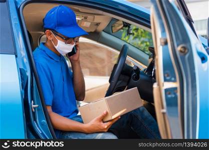 Asian delivery man courier online holding deliveries out boxes in car and using mobile phone contact the customer he protective face mask service under curfew quarantine pandemic coronavirus COVID-19