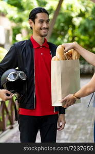 Asian delivery man pick up bakery grocery bag from bakery shop to deliver to customer who make online order. Online food delivery service concept in new normal after coronavirus pandemic.