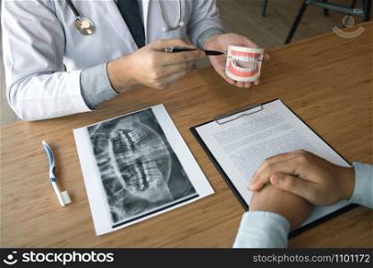 Asian dentist holding pen pointing to the dentures and is describing the problem of teeth.