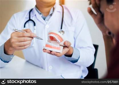 Asian dentist holding pen pointing to the dentures and is describing the problem of teeth.
