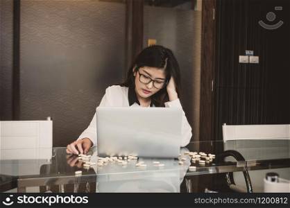 Asian depressed businesswoman with casual suit in seriuos action while working with computer laptop and take medicine in modern meeting room office, Business lifestyle and depress concept
