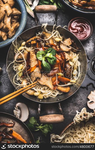 Asian dish with chicken vegetables noodle stir-fry in little wok with chopstick and cooking ingredients, top view