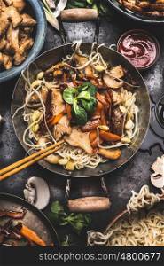 Asian dish with chicken vegetables noodle stir-fry in little wok with chopstick and cooking ingredients, top view