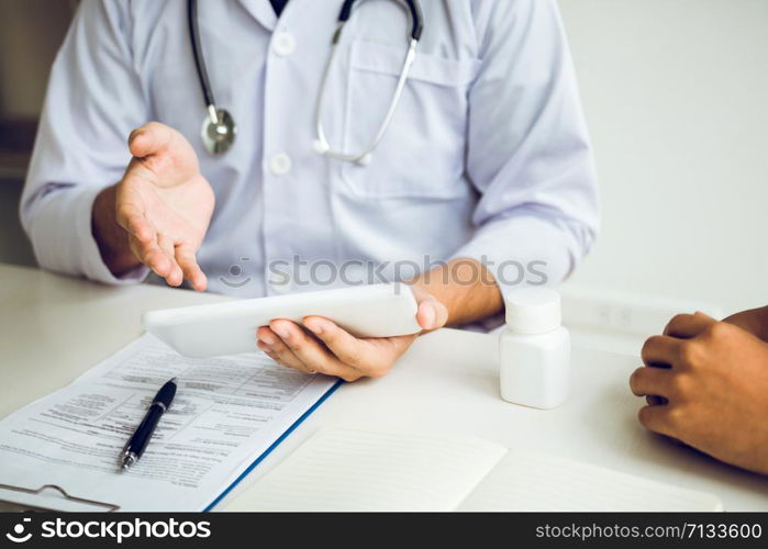 Asian doctor talking the patient at clinic while using the tablet explaining the patient condition and the treatment result.