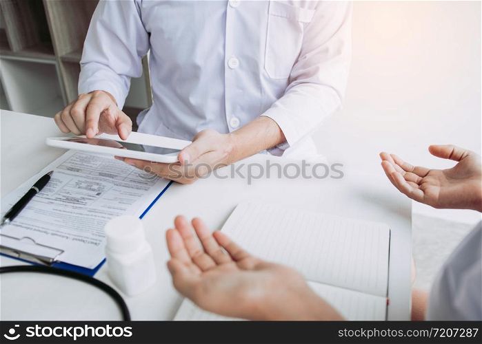 Asian doctor talking the patient at clinic while using the tablet explaining the patient condition and the treatment result.