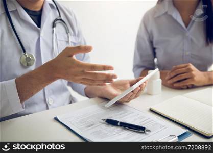 Asian doctor talking the patient at clinic while using the tablet explaining the patient condition and the treatment result.