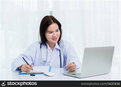 Asian doctor young beautiful woman smiling using working with a laptop computer and her writing something on paperwork or clipboard white paper at hospital desk office, Healthcare medical concept