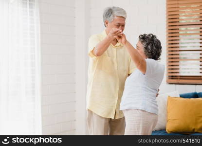 Asian elderly couple dancing together while listen to music in living room at home, sweet couple enjoy love moment while having fun when relaxed at home. Lifestyle senior family relax at home concept.