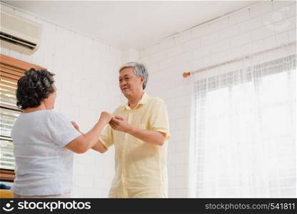 Asian elderly couple dancing together while listen to music in living room at home, sweet couple enjoy love moment while having fun when relaxed at home. Lifestyle senior family relax at home concept.
