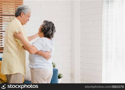 Asian elderly couple dancing together while listen to music in living room at home, sweet couple enjoy love moment while having fun when relaxed at home. Lifestyle senior family relax at home concept.