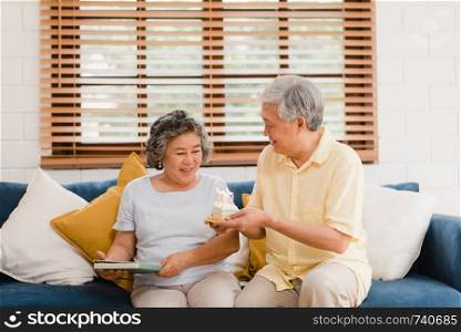 Asian elderly couple man holding cake celebrating wife's birthday in living room at home. Japanese couple enjoy love moment together at home. Lifestyle senior family at home concept.