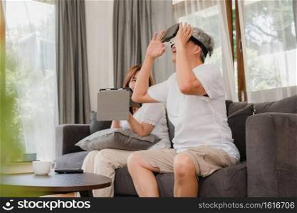 Asian elderly couple using tablet and virtual reality simulator playing games in living room, couple feeling happy using time together lying on sofa at home. Lifestyle Senior family at home concept.