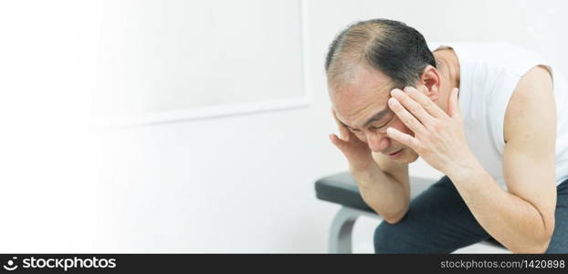 Asian Elderly man having headache while exercise. Stressed Senior male sitting on bench and having painful from migraine. Banner, Panoramic, copy space.