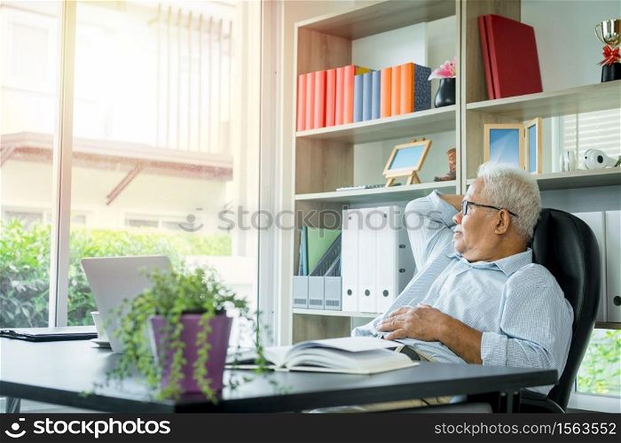 Asian elderly man sitting in front of a laptop computer, He is sitting back in his chair and relax. The elderly can still work And create sentences for society, virus quarantine,