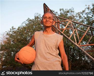 Asian elderly men in sportswear holding a basketball and looking at the camera at an outdoor basketball court on summer day. Healthy lifestyle and Healthcare concept.