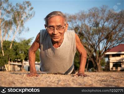 Asian elderly men with gray hair in sportswear doing push ups in the park on summer day. Healthy lifestyle and Healthcare concept.