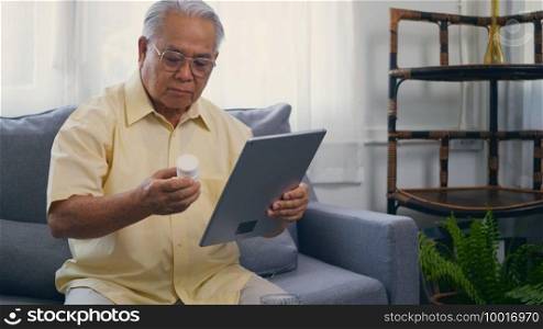Asian elderly patient video call by digital tablet to doctor for inquire about which bottle of medication pills should be taken in living room at home,  Senior old man technology online healthcare