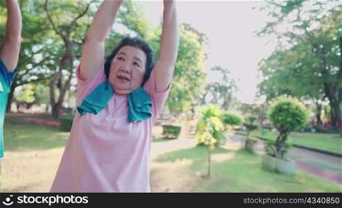 Asian elderly people doing group stretching warm up exercise inside the park, over head arm extension stretch, senior health care insurance, outdoor activities, vitality wellness fitness instructor
