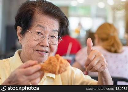 Asian elderly women are eating fried chicken. In the restaurant And lift the thumb. Her smile and look happy. Concept of aging society, Preparedness After retirement And living a happy life.