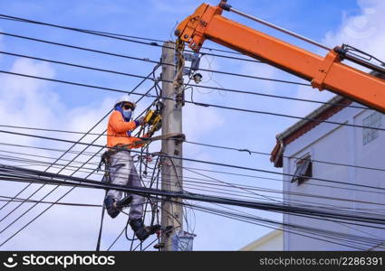 Asian electrician in protective mask with crane truck is installing cable lines and electrical transmission on electric power pole against blue sky background