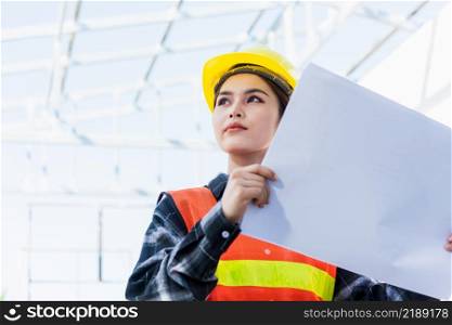 Asian engineer architect worker woman holding blueprint infrastructure progress at construction site, engineering female leader standing hold paper plan control worker to building project