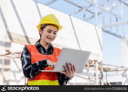 Asian engineer architect worker woman holding laptop inspect and oversee infrastructure progress at construction site, engineering use computer to operate project and control worker to building