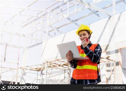 Asian engineer architect worker woman working at build construction site use laptop and talking with radio, engineering hold computer and radio discuss operate and control worker employee to building