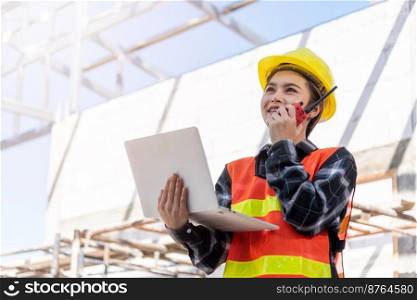 Asian engineer architect worker woman working at build construction site use laptop and talking with radio, engineering hold computer and radio discuss operate and control worker employee to building