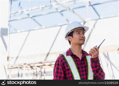 Asian engineer foreman architect worker man working at building construction site talking with radio, engineering hold radio discuss operate and control worker employee to building construction