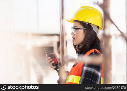 Asian engineer foreman architect worker woman working at building construction site talking with radio, engineering hold radio discuss operate and control worker employee to building construction