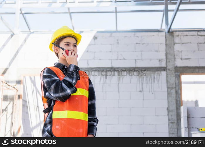 Asian engineer foreman architect worker woman working at building construction site talking with radio, engineering hold radio discuss operate and control worker employee to building construction