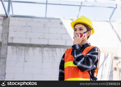 Asian engineer foreman architect worker woman working at building construction site talking with radio, engineering hold radio discuss operate and control worker employee to building construction