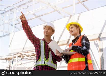 Asian engineer foreman worker man and woman working at building construction site use laptop and talking with radio, engineering hold computer and radio discuss and control worker employee to building