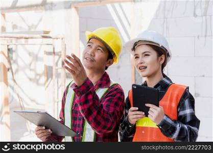 Asian engineer foreman worker man and woman working at building construction site use tablet talking to checking, engineering hold clipboard and discuss and control worker employee to building