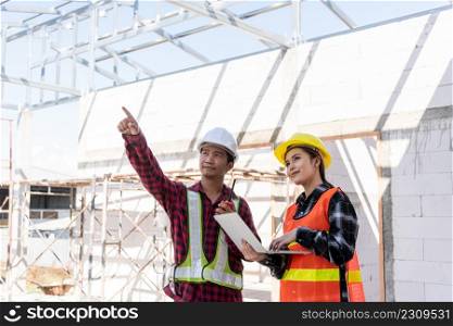 Asian engineer foreman worker man and woman working at building construction site use laptop and talking with radio, engineering hold computer and radio discuss and control worker employee to building