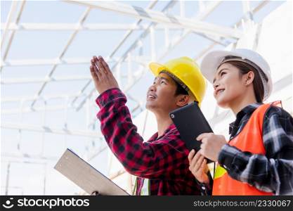 Asian engineer foreman worker man and woman working at building construction site use tablet talking to checking, engineering hold clipboard and discuss and control worker employee to building