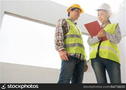 Asian engineer or Young Female Architect put on a helmet for safety and talk with a contractor on a construction building factory project, Concept of Teamwork, Leadership concept.