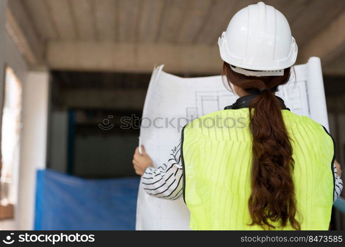 Asian engineer or Young woman Architect put on a helmet for safety and look at Blueprint for Inspect Building factory Construction Site on a construction site. Smart working woman concept.