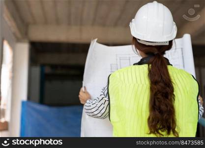 Asian engineer or Young woman Architect put on a helmet for safety and look at Blueprint for Inspect Building factory Construction Site on a construction site. Smart working woman concept.