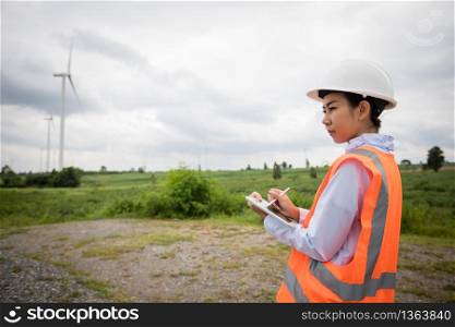 Asian engineer with hardhat using tablet pc computer inspecting and working at wind turbine farm Power Generator Station