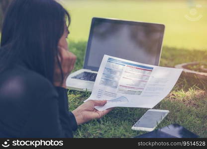 Asian entrepreneur business woman reading business graph analyze chart using laptop on green garden at home. Freelance working home office social distance new normal lifestyle in open cafe green park