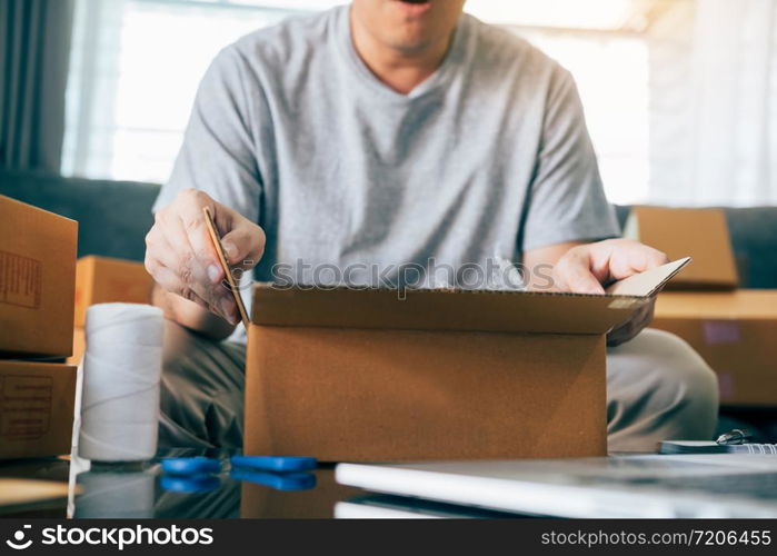 Asian entrepreneur teenager is opening a cardboard box in order to put the product that the customer ordered into the box to deliver the product.