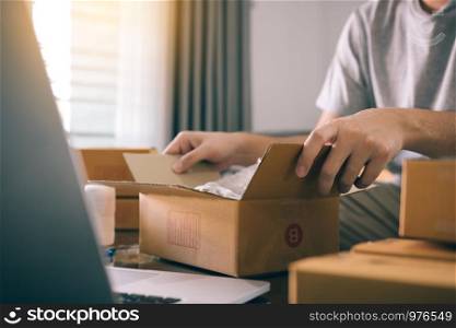 Asian entrepreneur teenager is opening a cardboard box in order to put the product that the customer ordered into the box to deliver the product.