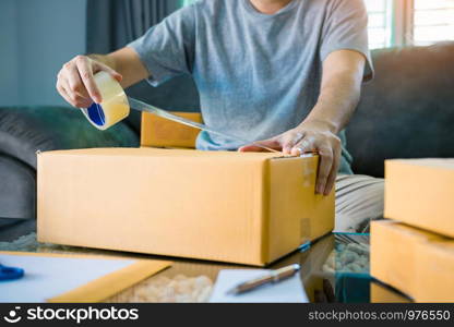 Asian entrepreneur teenagers are using the tape to seal the box by packing the product to send to customers.