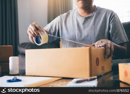 Asian entrepreneur teenagers are using the tape to seal the box by packing the product to send to customers.