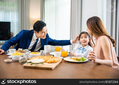 Asian family father, mother with children daughter eating breakfast food on dining table kitchen in mornings together at home before father left for work, happy couple family