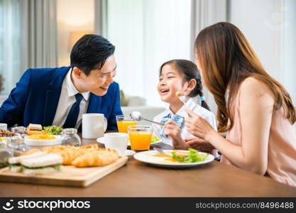 Asian family father, mother with children daughter eating breakfast food on dining table kitchen in mornings together at home before father left for work, happy couple family