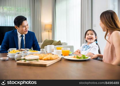 Asian family father, mother with children daughter eating breakfast food on dining table kitchen in mornings together at home before father left for work, happy couple family